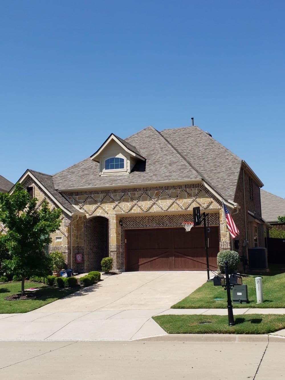 Two-story brick house with a stone facade, landscaped yard, and American flag on a sunny day.