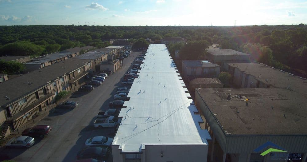 Aerial view of a residential area with parked cars and a newly renovated white roof.