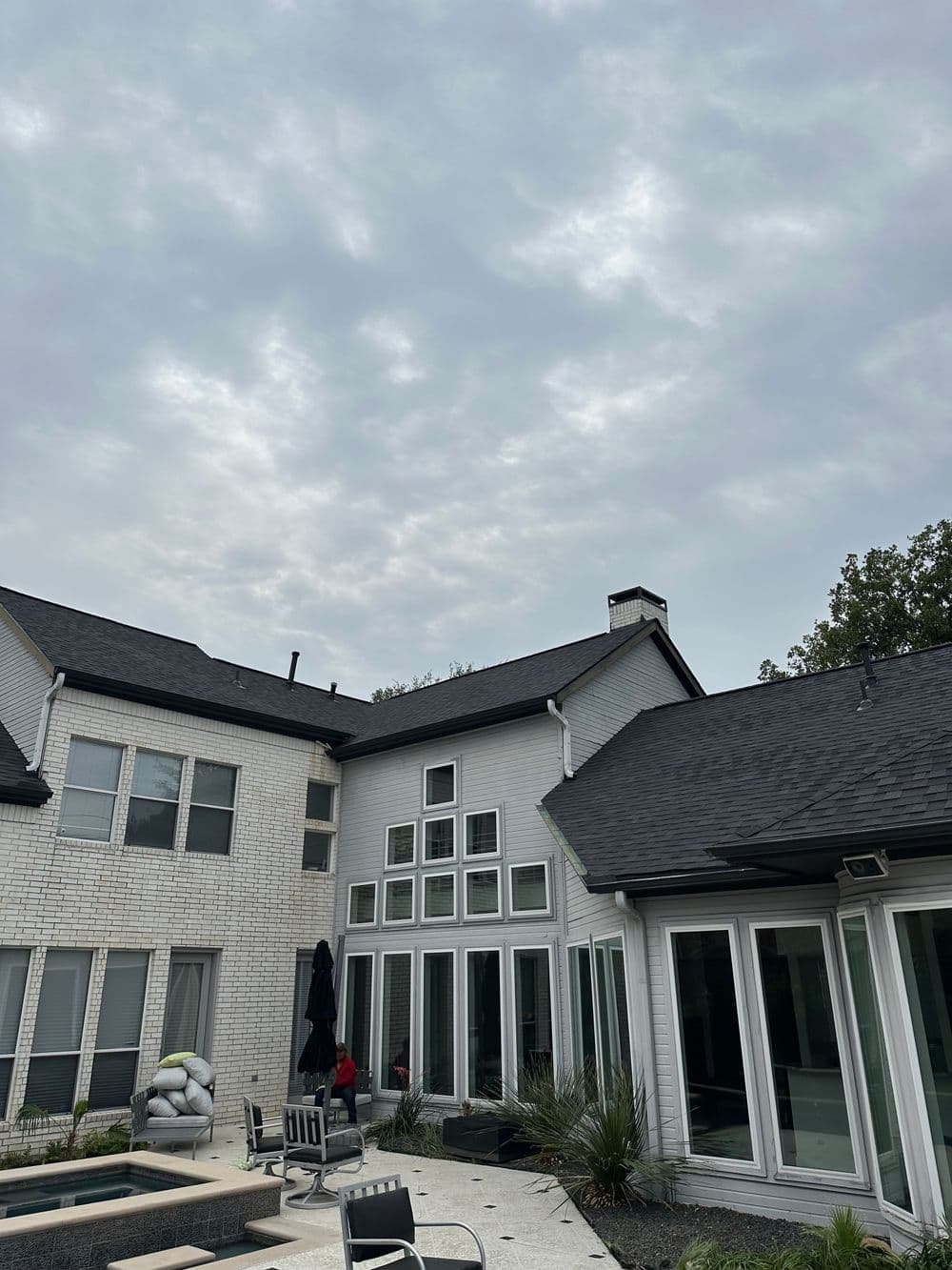Modern house exterior with large windows, pool, and overcast sky in the background.