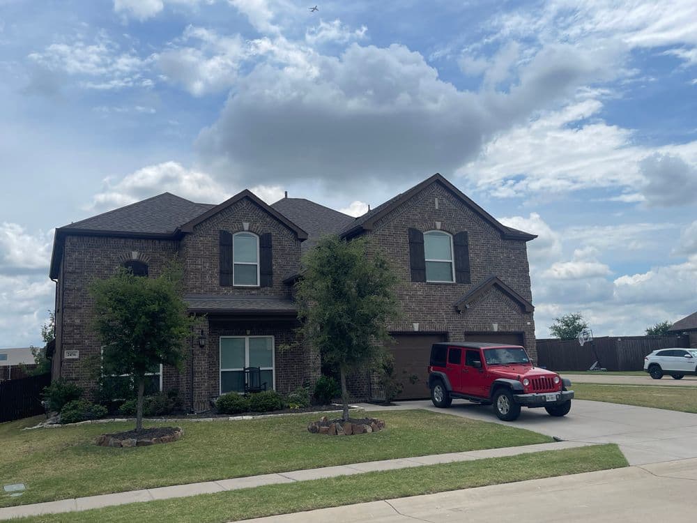 Two-story brick house with a red Jeep parked in the driveway under a cloudy sky.