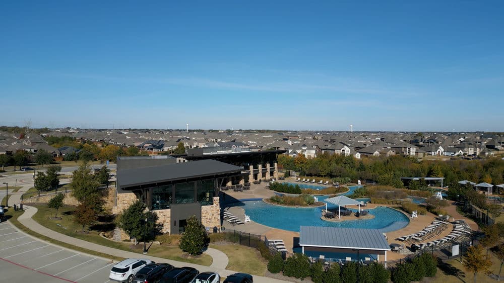 Aerial view of a modern resort-style pool and clubhouse surrounded by residential homes.